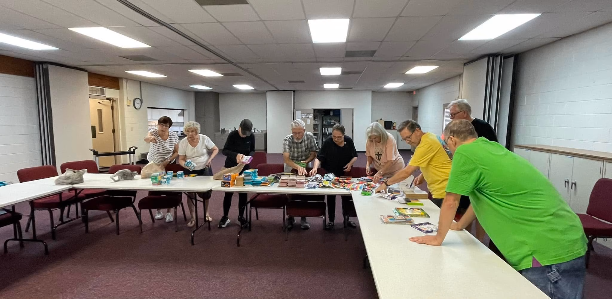 Volunteers gathered around long tables in the fellowship hall, sorting donated school supplies and toiletries into groups.