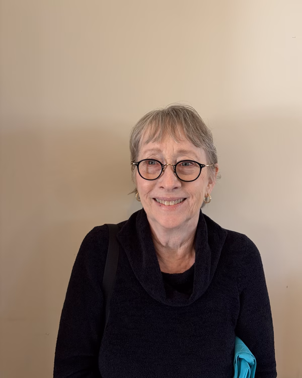 Jan Schultz, smiling, with short grey hair and round tortoiseshell glasses, wearing a black cowl-neck sweater.