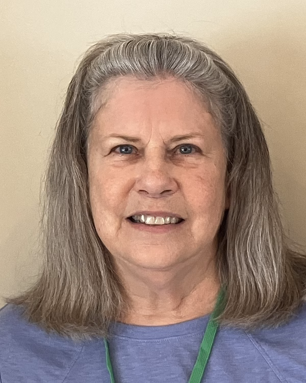 Kim Barry, smiling, with long grey hair and a light periwinkle top.