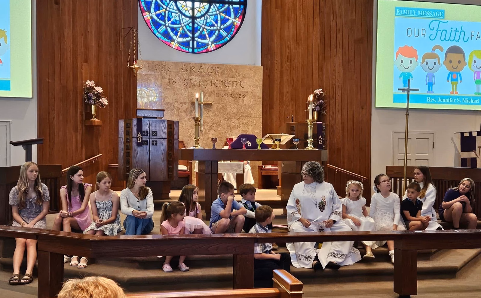 Children and youth of all ages seated along the chancel steps at the communion rail during the Family Message, with the pastor seated among them in white vestments